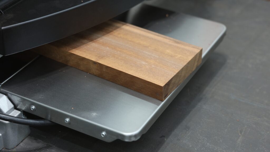 Close-up of a sapele board exiting the planer with a clean, snipe-free edge