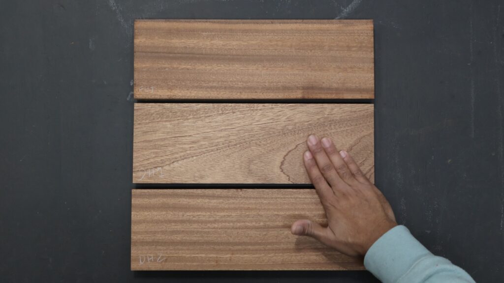 Three sapele boards showing smooth surface quality after planing, with a hand inspecting the middle board.