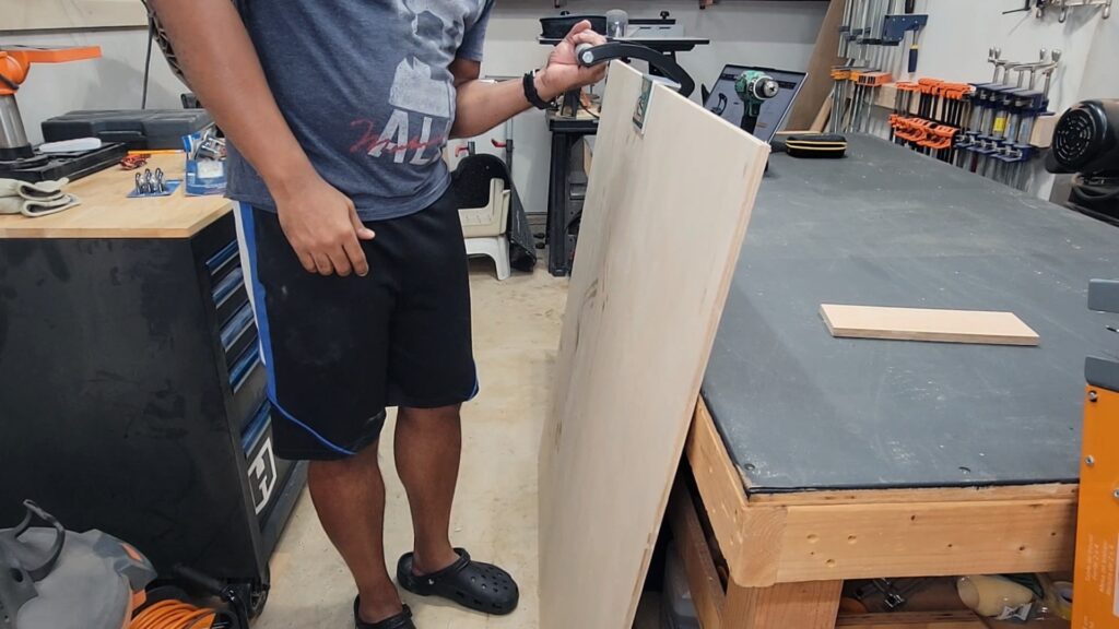 Person carrying plywood sheet with panel carrier handle tool in workshop